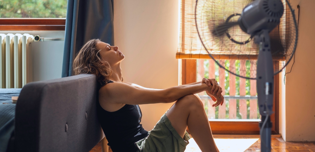 woman resting in front of fan on the floor of her home in the summer heat