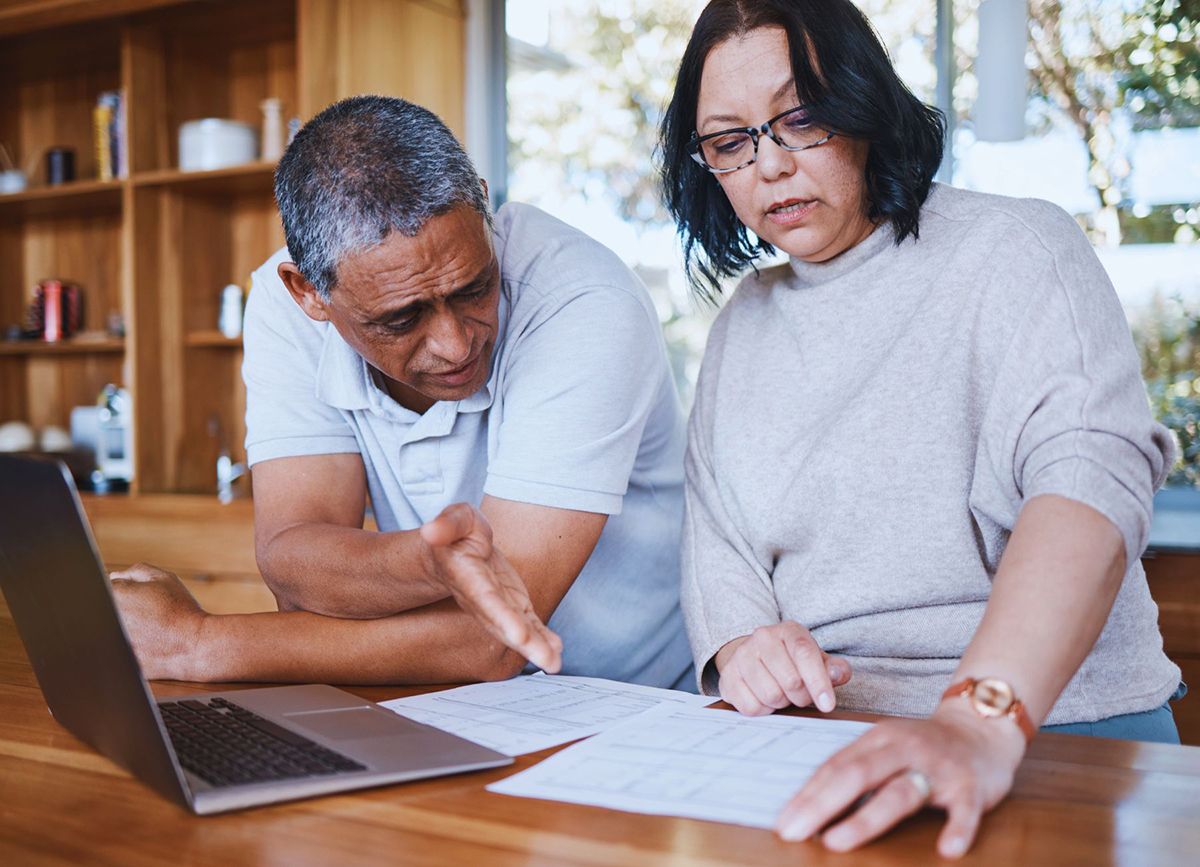 Mature couple stressed at finances and rising energy costs in home looking at bills in kitchen