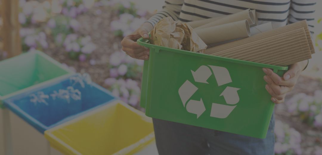 Close-up of a green basket with a recycling symbol with papers held by a woman