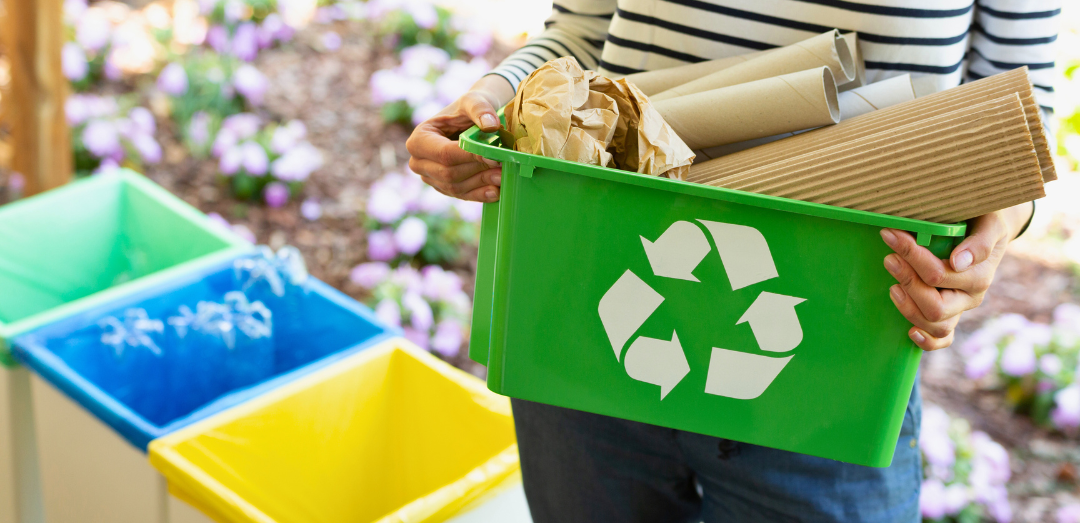 Close-up of a green basket with a recycling symbol with papers held by a woman