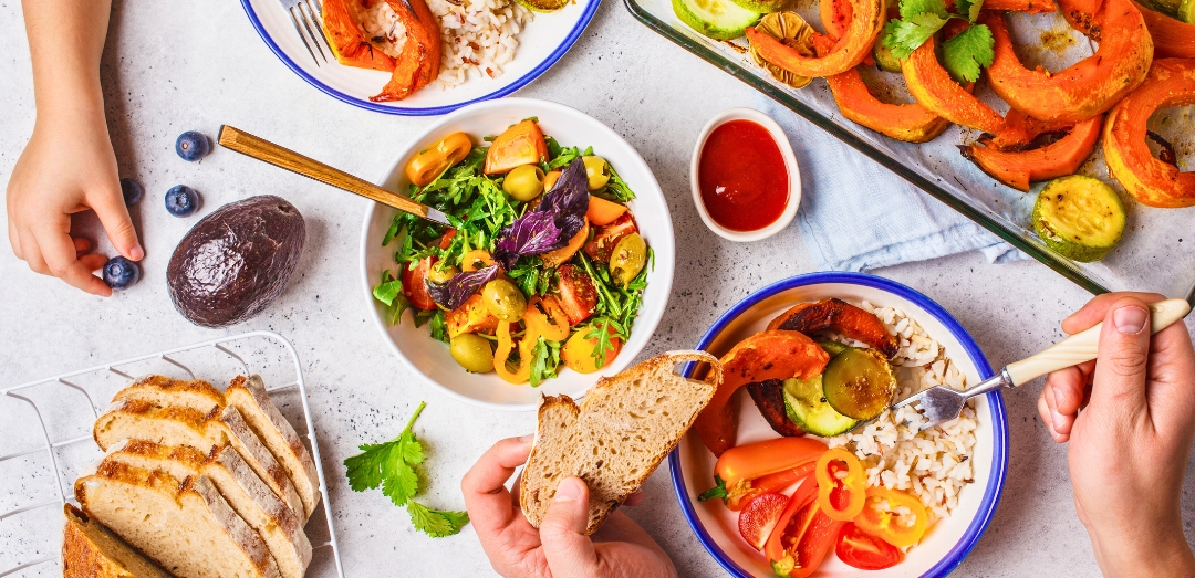 Flat lay of family hands eating healthy food. Vegan lunch table top view. Baked vegetables, fresh salad, berries, bread on a white background.