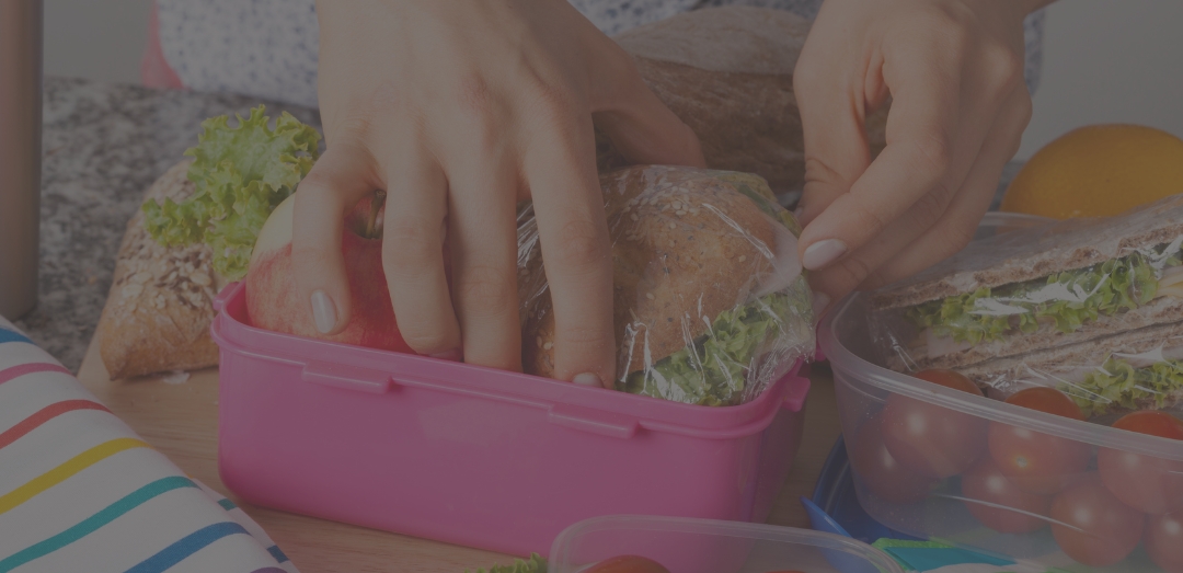 close-up of woman packing lunch sandwich vegetables in plastic Tupperware with metal water bottle to side